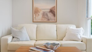 A living room with a beige sofa, a wooden coffee table, and a framed picture of a beach path. - Seascape Studio in Terrigal (Terrigal)