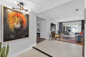 A modern living room with a large painting of a lion's face on the wall, a sofa, a coffee table, and a view of the outdoors through large windows. - Sun, Pool & Sand- Fort Lauderdale Style Escape! (Fort Lauderdale)