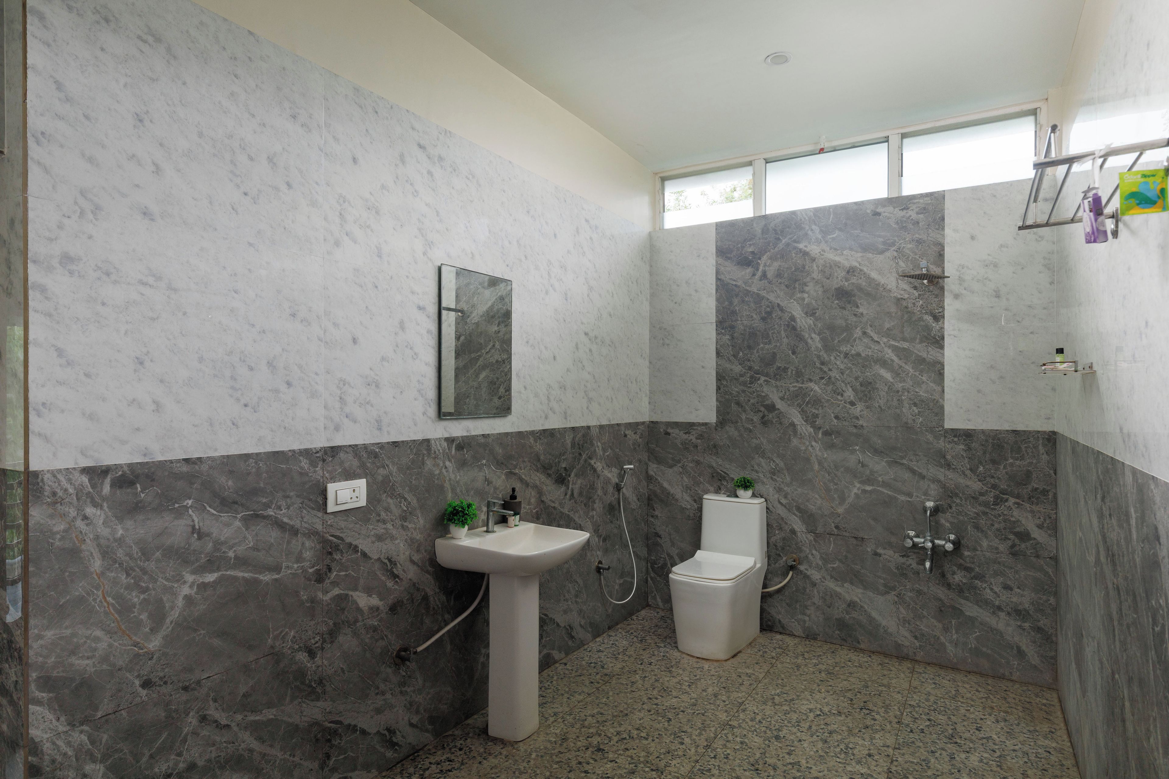 Baño con lavamanos, inodoro y zona de ducha, con paredes de mármol y ventanal.