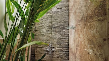 A stone wall with a built-in shower and a small garden area with tropical plants.