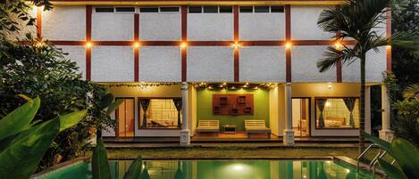 A hotel with a pool, a covered seating area, and a well-lit facade.