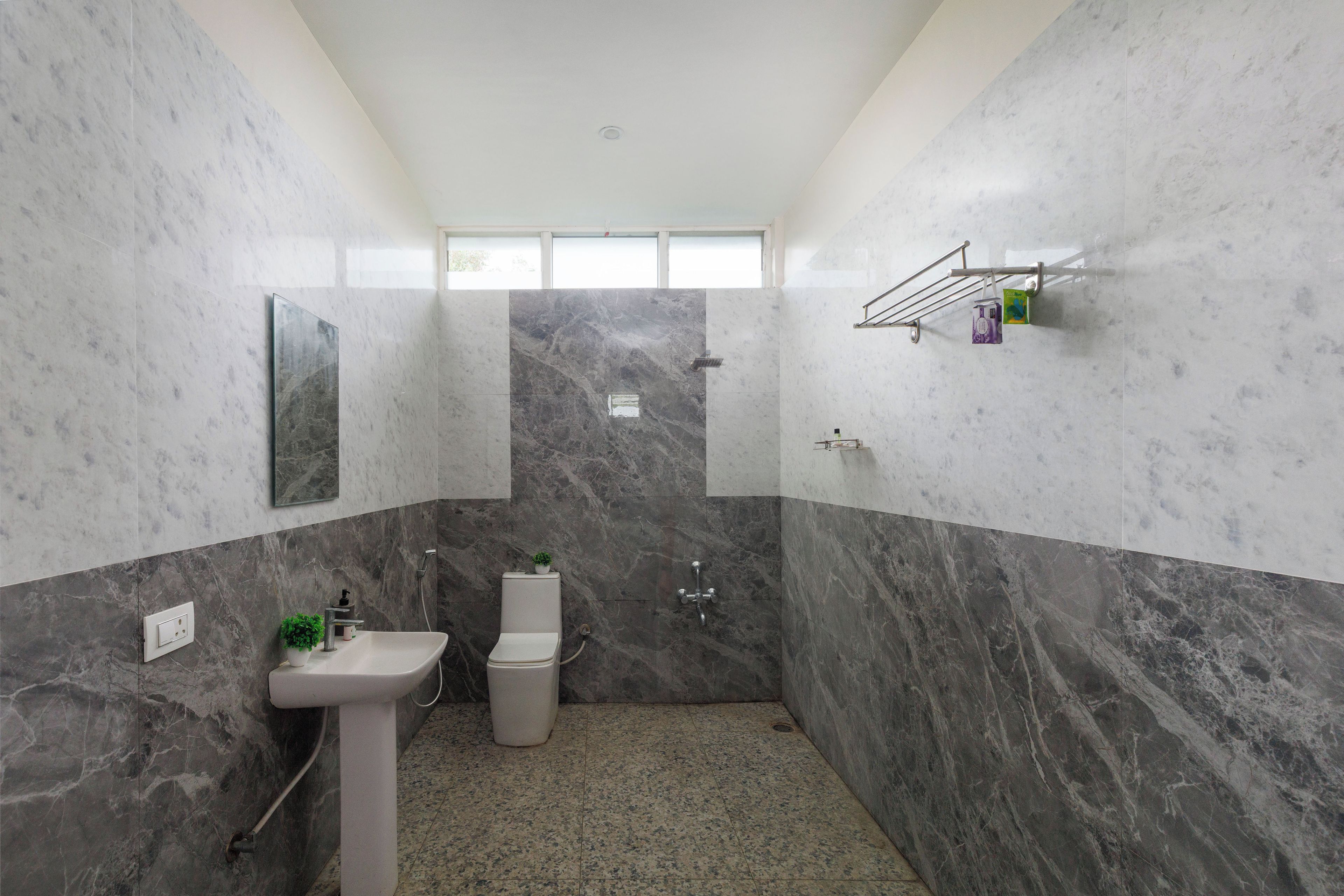 Een badkamer met een marmeren wand, een wastafel, toilet en douche.