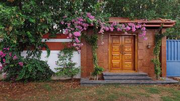 A wooden door with a small porch and steps leading up to it, surrounded by greenery and flowering plants.