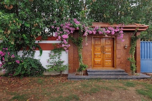 A wooden door with a small porch and steps leading up to it, surrounded by greenery and flowering plants.