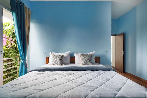 A bedroom with a bed, two pillows, a bedside table, a clock, and a door.