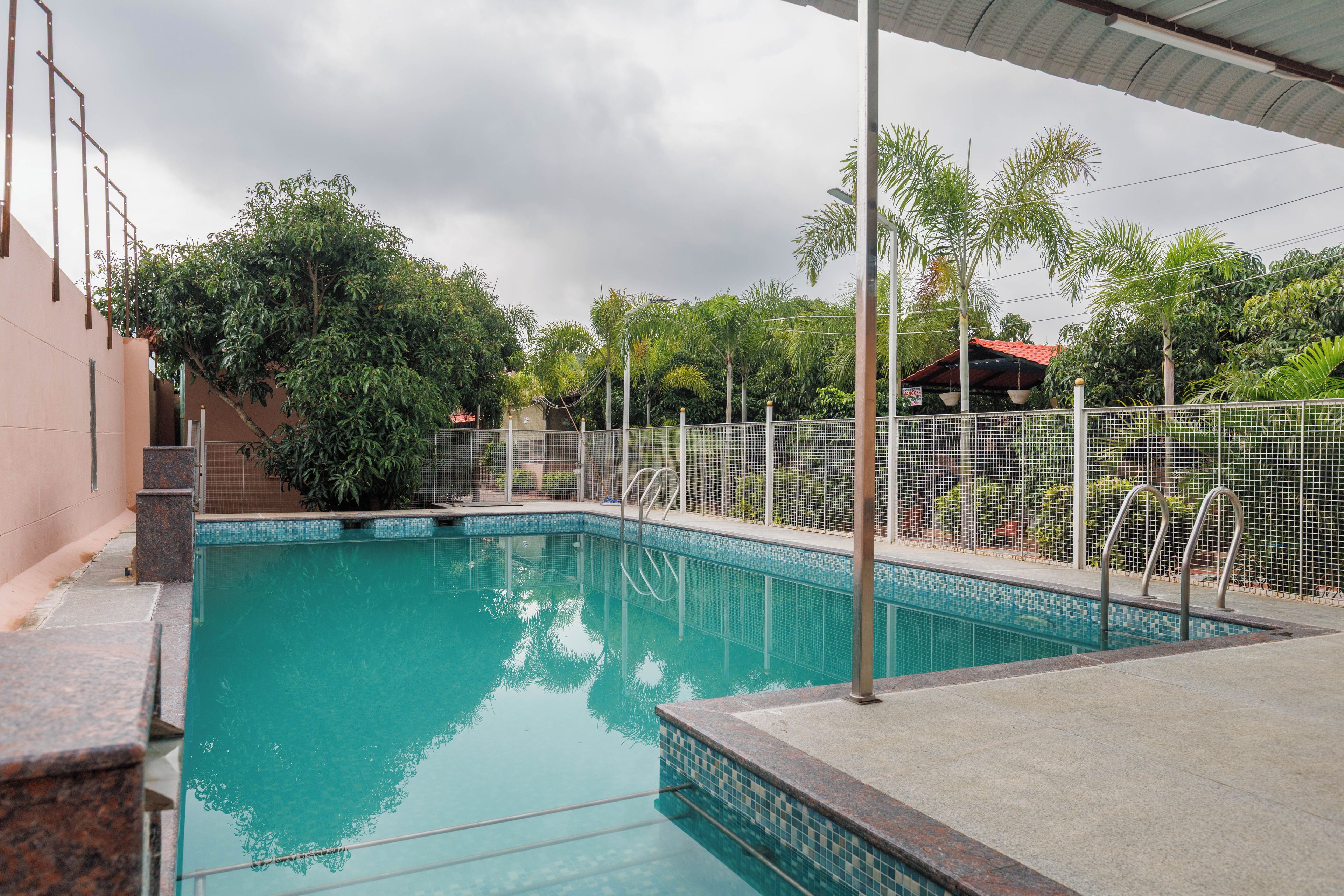 Una piscina con borde de azulejos, rodeada de una valla y árboles.