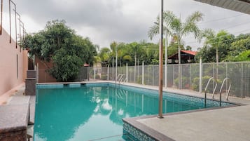Una piscina con borde de azulejos, rodeada de una valla y árboles.