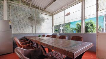 Un salón de conferencias con una larga mesa y sillas, un refrigerador y un ventanal con vistas a la vegetación.