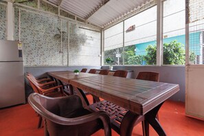 A conference room with a long table and chairs, a refrigerator, and a window with a view of greenery. - White Swan by Stayjadepoolbbqbonfire Mysore Rd (Ramanagara)