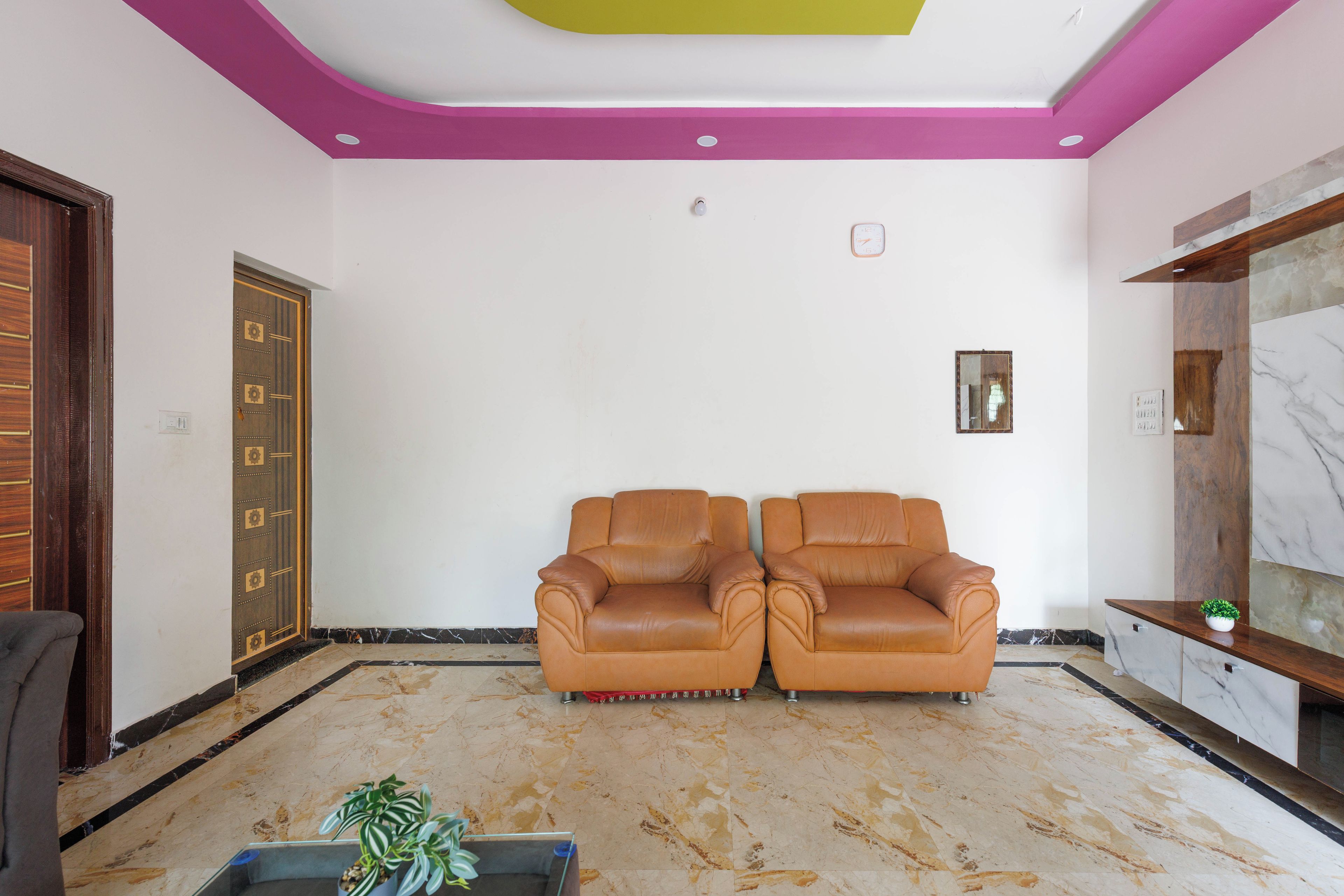 A room with two leather sofas, a wooden door, and a marble floor.