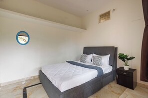 A bedroom with a bed, a nightstand, a potted plant, and a wall-mounted mirror.