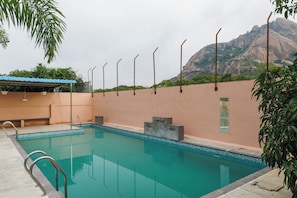 A swimming pool with a clear blue water, surrounded by a low wall and a mountain in the background. - White Swan by Stayjadepoolbbqbonfire Mysore Rd (Ramanagara)