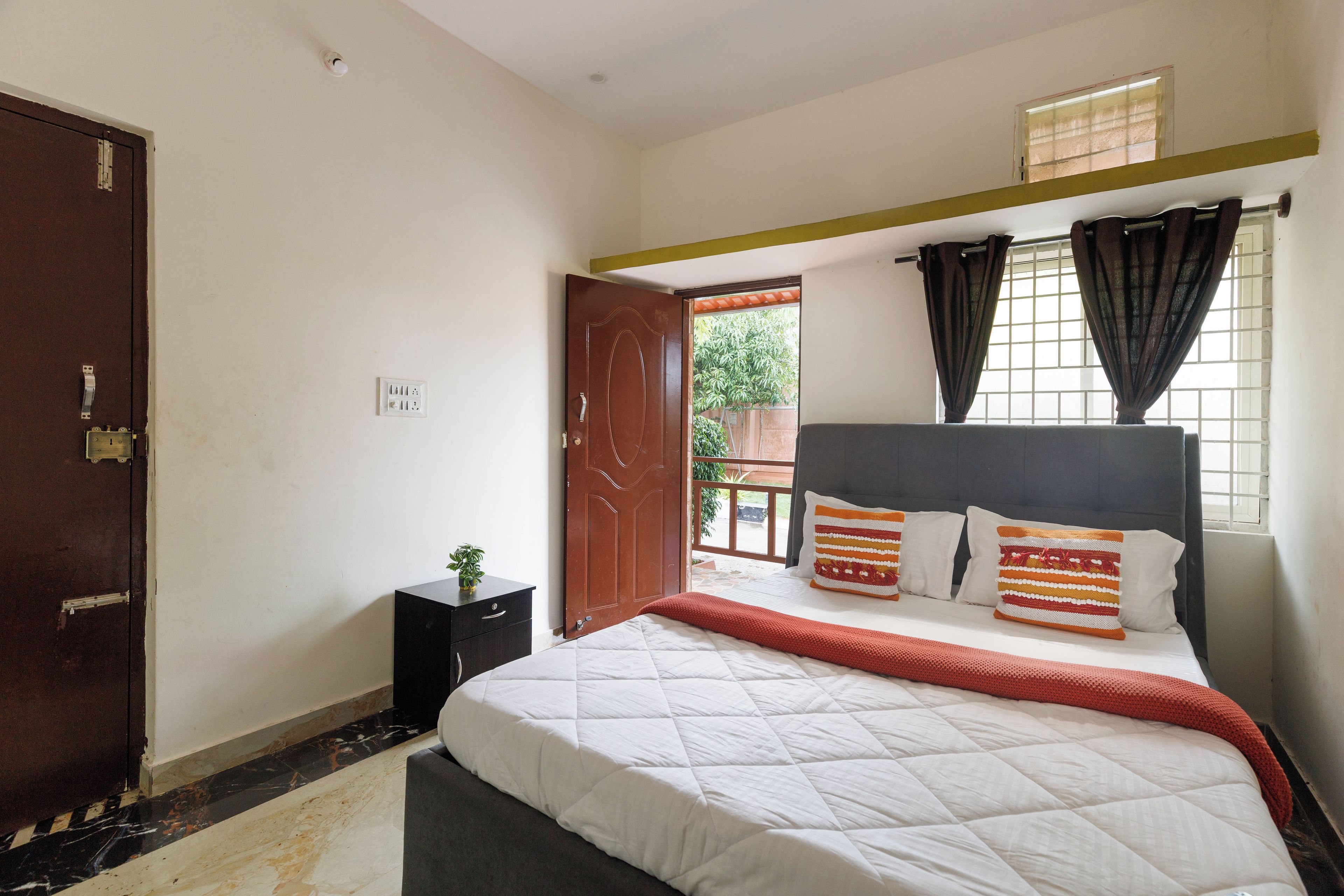 A bedroom with a bed, a nightstand, a window with curtains, and a door.