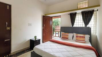 A bedroom with a bed, a nightstand, a window with curtains, and a door.