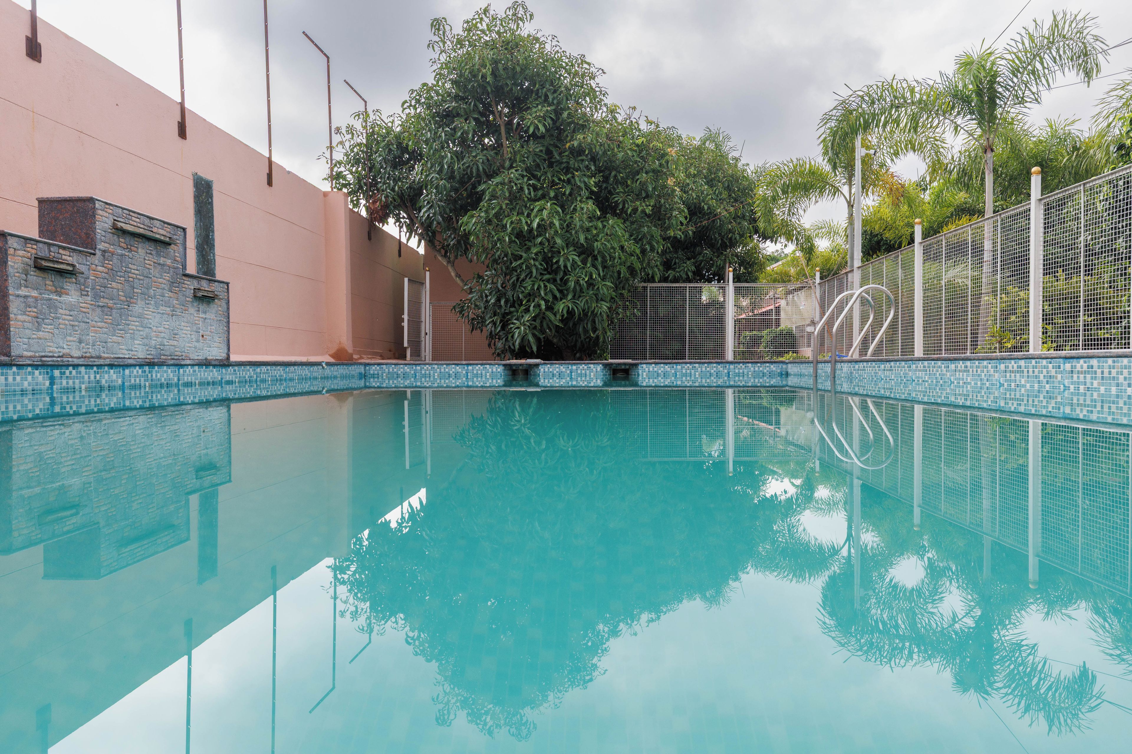 Una piscina cristalina con borde de azulejos, rodeada de una valla y árboles.