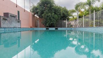 Una piscina cristalina con borde de azulejos, rodeada de una valla y árboles.