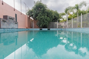A clear swimming pool with a tiled edge, surrounded by a fence and trees.