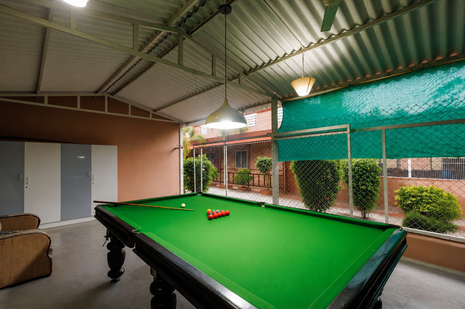 A pool table with balls, a hanging light fixture, and a view of a fenced outdoor area with greenery.