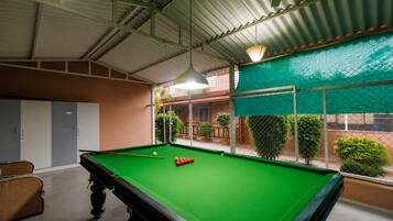 A pool table with balls, a hanging light fixture, and a view of a fenced outdoor area with greenery.