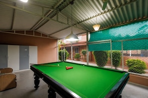 A pool table with balls, a hanging light fixture, and a view of a fenced outdoor area with greenery.