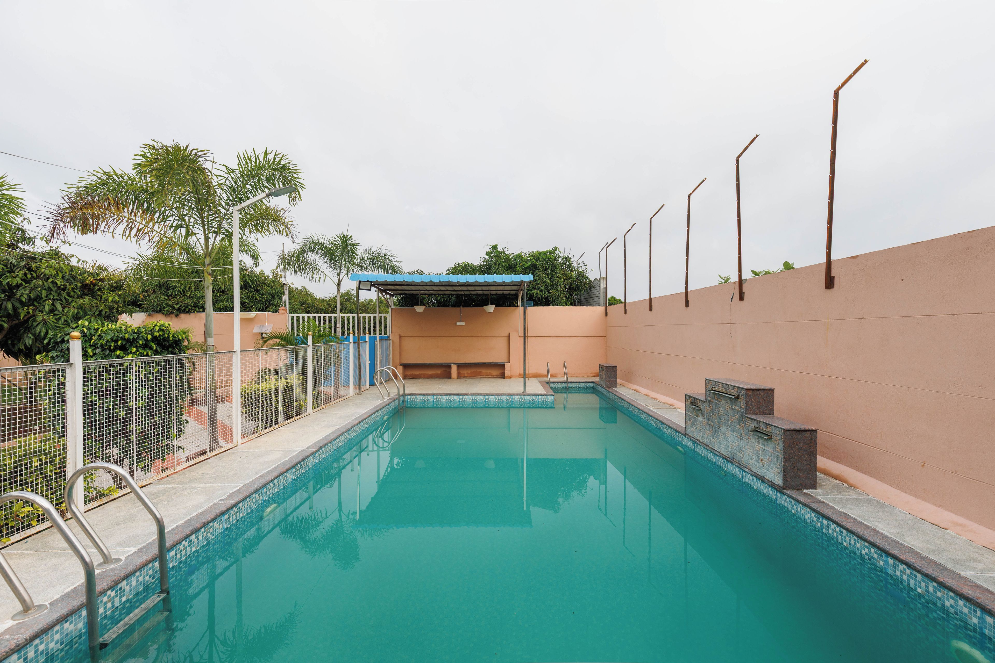 A swimming pool with a tiled edge, a metal ladder, and a covered area with a blue roof.