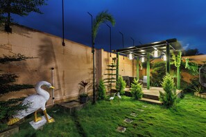 A well-maintained garden with a swan statue, a patio area with seating, and a variety of plants. - White Swan by Stayjadepoolbbqbonfire Mysore Rd (Ramanagara)