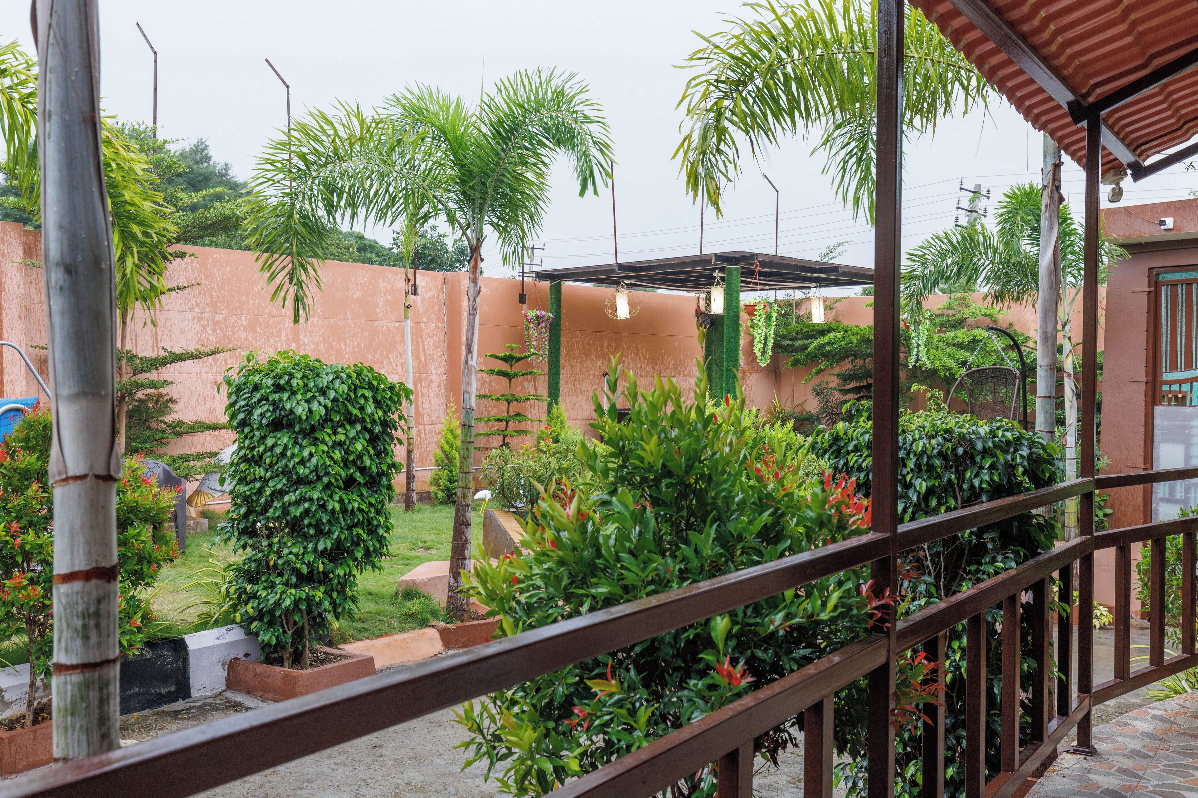 A covered outdoor area with a metal railing, surrounded by various plants and a brick wall.