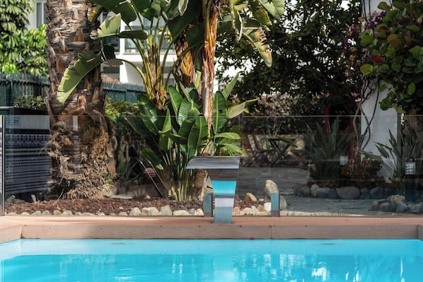 Una piscina con superficie de agua azul cristalina, rodeada de plantas tropicales y una estructura metálica.