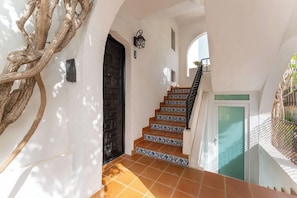 Una escalera con baldosas estampadas que conduce a una puerta, una lámpara de pared y una estructura de madera decorativa.