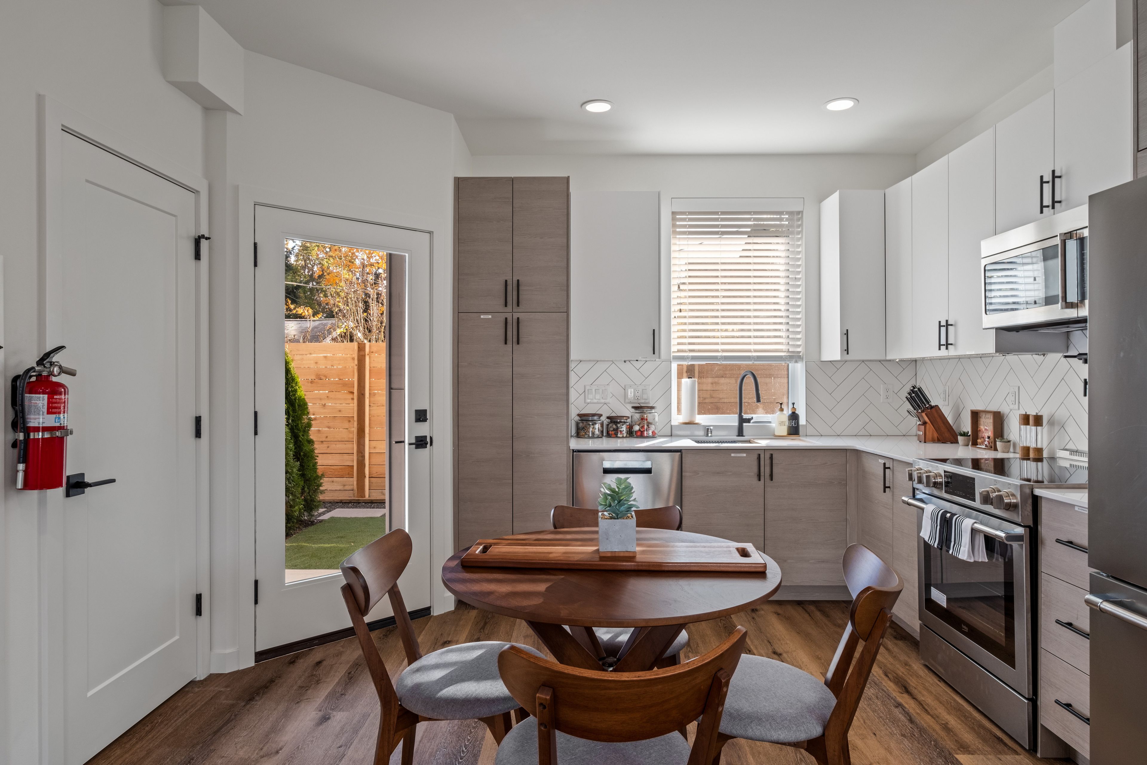 A modern kitchen with white cabinets, a stainless steel oven, and a dining area with a wooden table and chairs.
