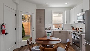 A modern kitchen with white cabinets, a stainless steel oven, and a dining area with a wooden table and chairs.