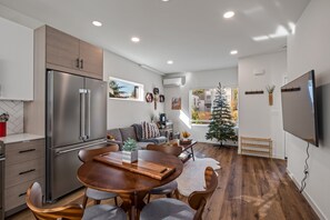 Une cuisine moderne dotée d’un réfrigérateur encastré, un coin repas avec une table et des chaises en bois, et un espace de vie comprenant un canapé et un sapin de Noël.