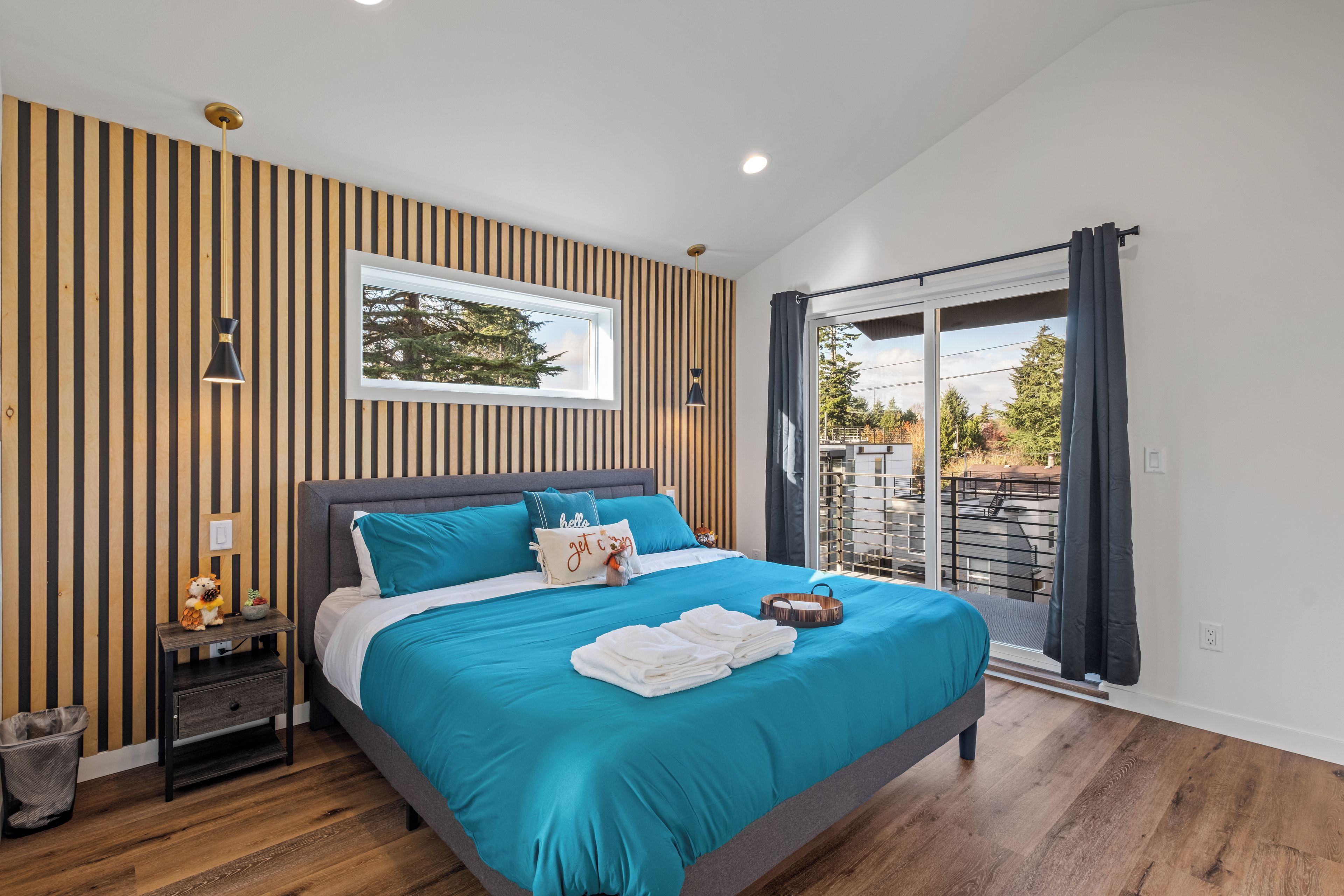 A modern bedroom with a large bed, a nightstand, a window, and a view of the outdoors.