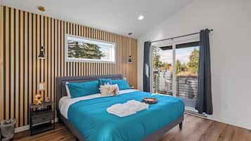 A modern bedroom with a large bed, a nightstand, a window, and a view of the outdoors.