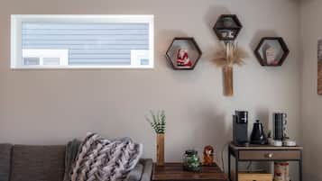 A living room with a window, a couch, a coffee table, a decorative plant, and a coffee machine.