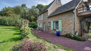 Ein Steinhaus mit Kiesauffahrt, ein kleiner Garten mit blühenden Pflanzen und eine Holzterrasse.