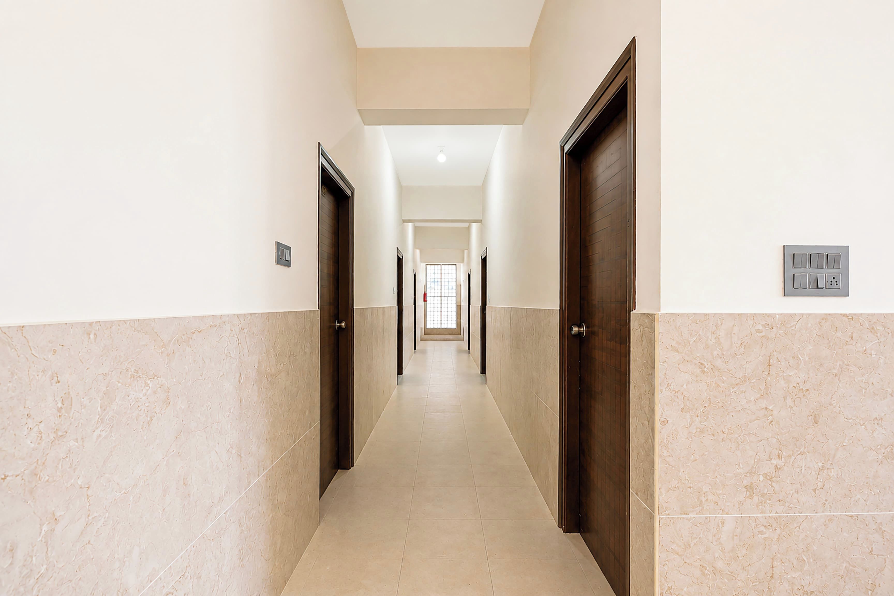 Un pasillo con puertas a ambos lados, un interruptor de luz en la pared y un suelo de baldosas.