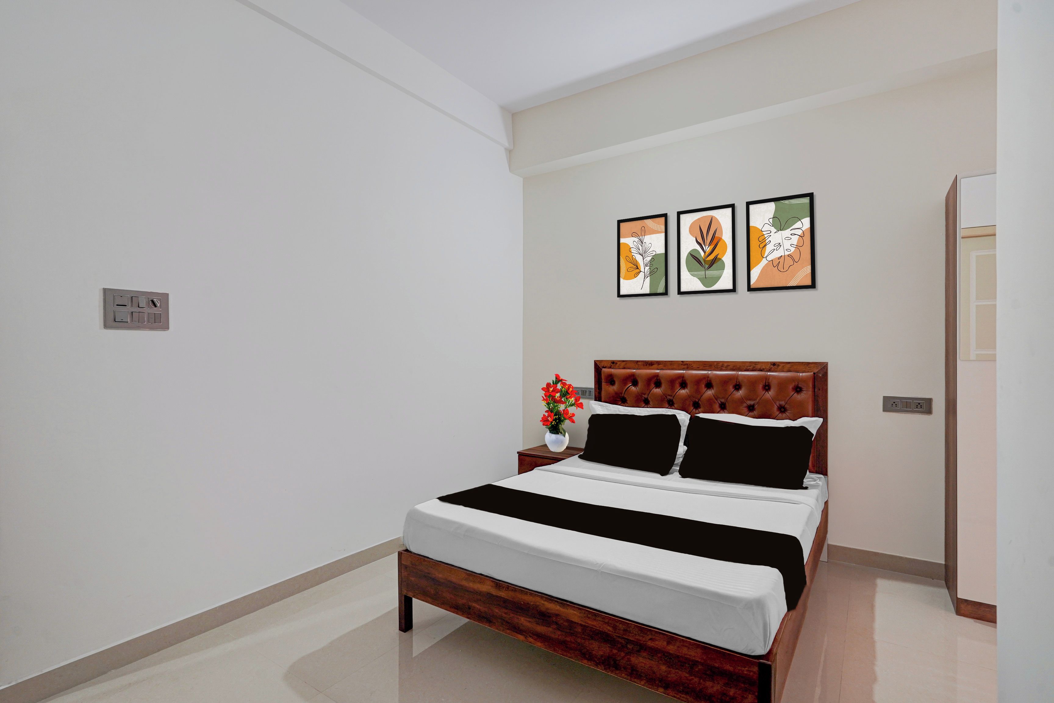 Una habitación de hotel con una cama, una mesita de noche, un florero con flores y tres cuadros enmarcados en la pared.