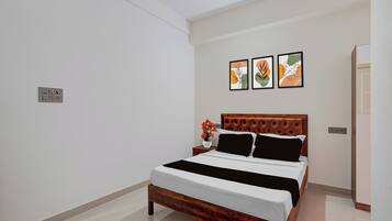Una habitación de hotel con una cama, una mesita de noche, un florero con flores y tres cuadros enmarcados en la pared.