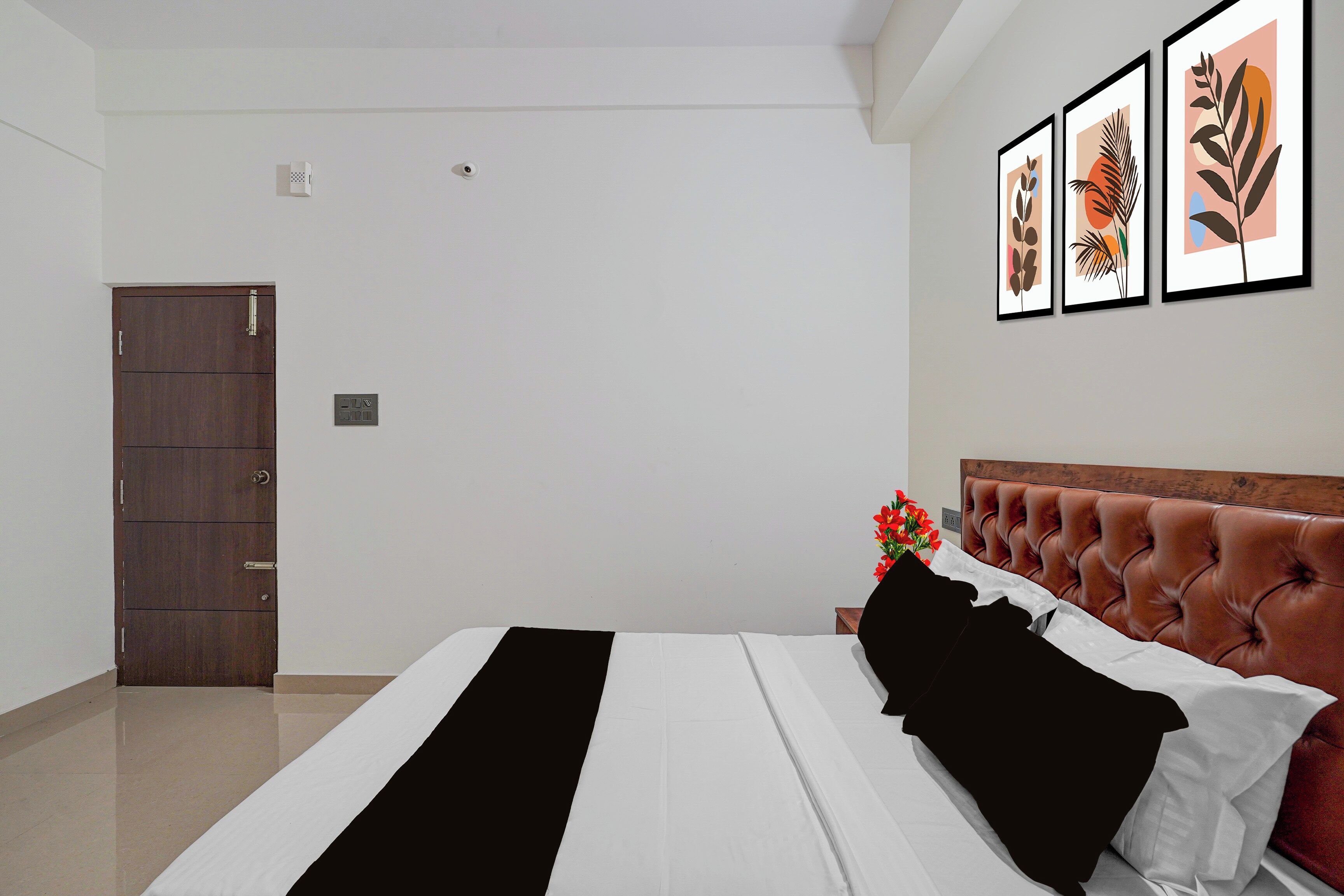 Ein Schlafzimmer mit einem Bett, einem Holzschrank, einem Nachttisch mit Blumenvase und drei gerahmten Kunstwerken an der Wand.