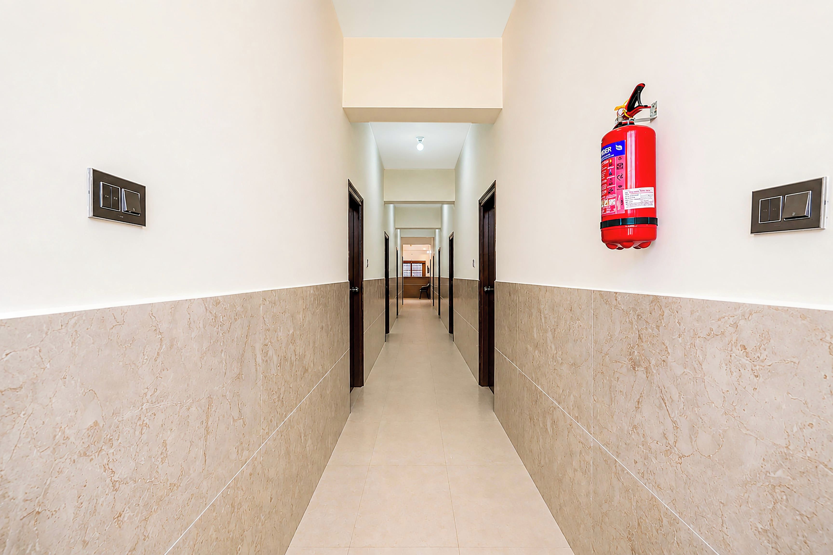Un pasillo con un extintor en la pared, puertas a ambos lados y suelo de baldosas.