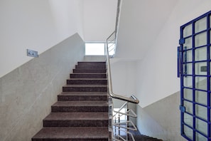 A staircase with a metal handrail and a blue door at the bottom. - Collection O Magadi Road Metro Station (Nelamangala)