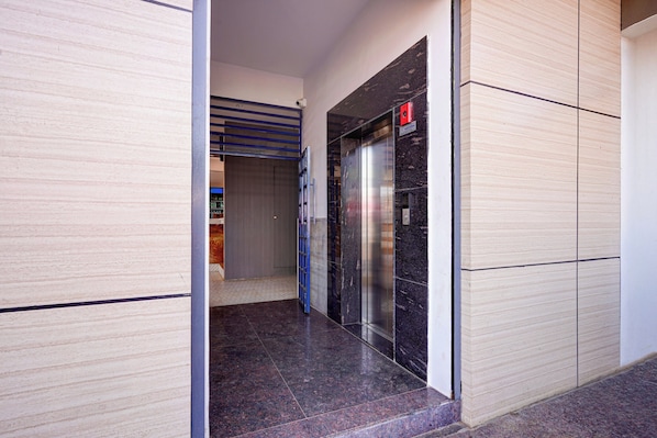 A hallway with a closed elevator and a door leading to a room with a tiled floor. - Collection O Magadi Road Metro Station (Nelamangala)