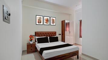 A bedroom with a wooden bed, a nightstand with a vase of flowers, and three framed pictures on the wall.