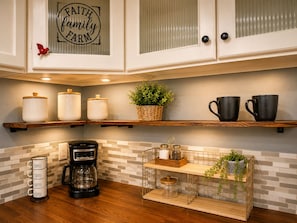 Una cocina con armarios blancos, repisas de madera, una cafetera y objetos decorativos.