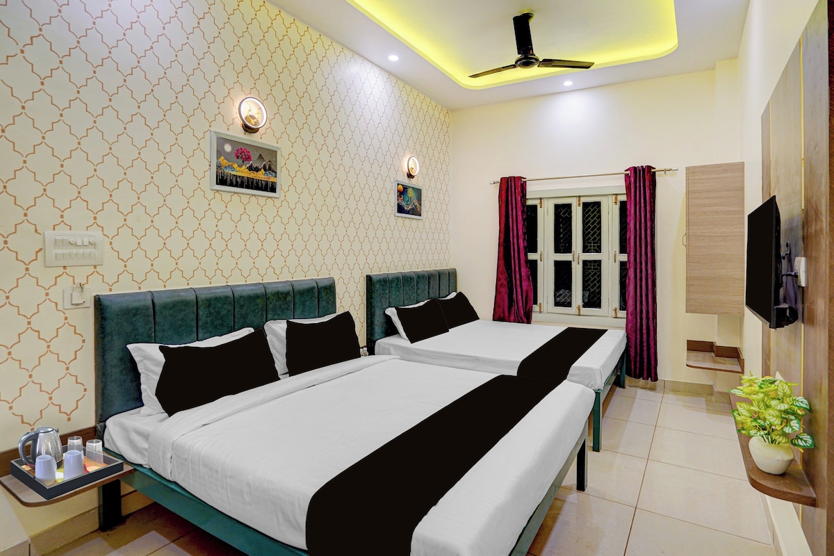 A hotel room with two beds, a ceiling fan, a window with curtains, and a television on the wall.