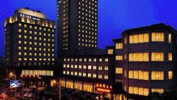 A multi-story building with illuminated windows, a parking lot, and a street with vehicles.