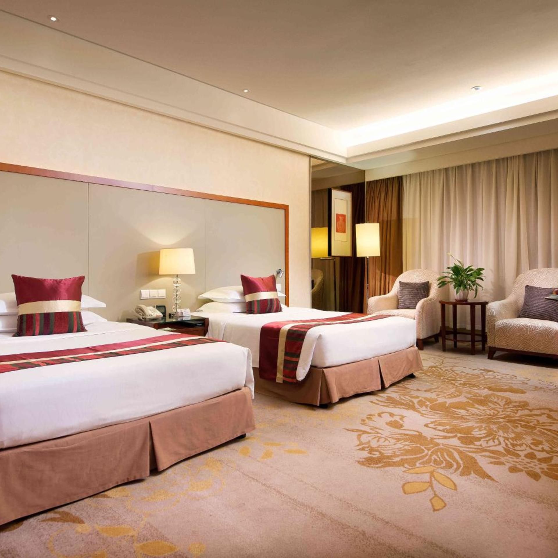 A hotel room with two beds, a sitting area with a chair and a table, and a large mirror on the wall.