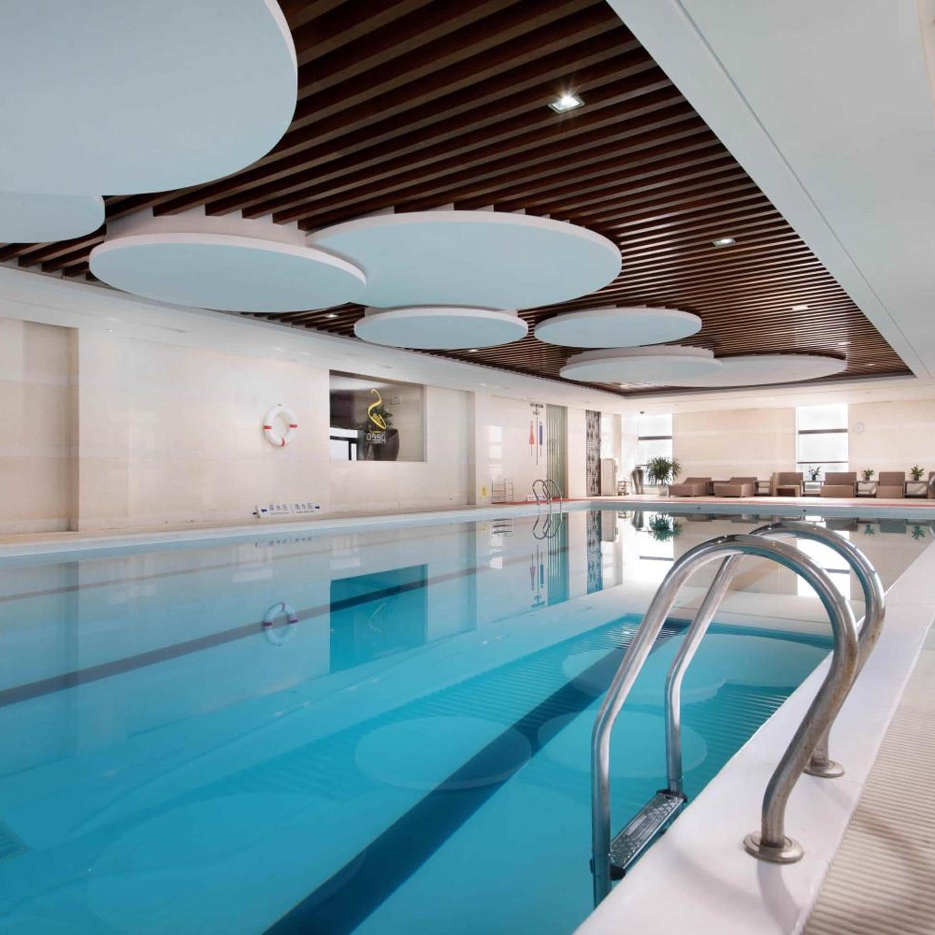 An indoor swimming pool with a wooden ceiling and a seating area with sofas.