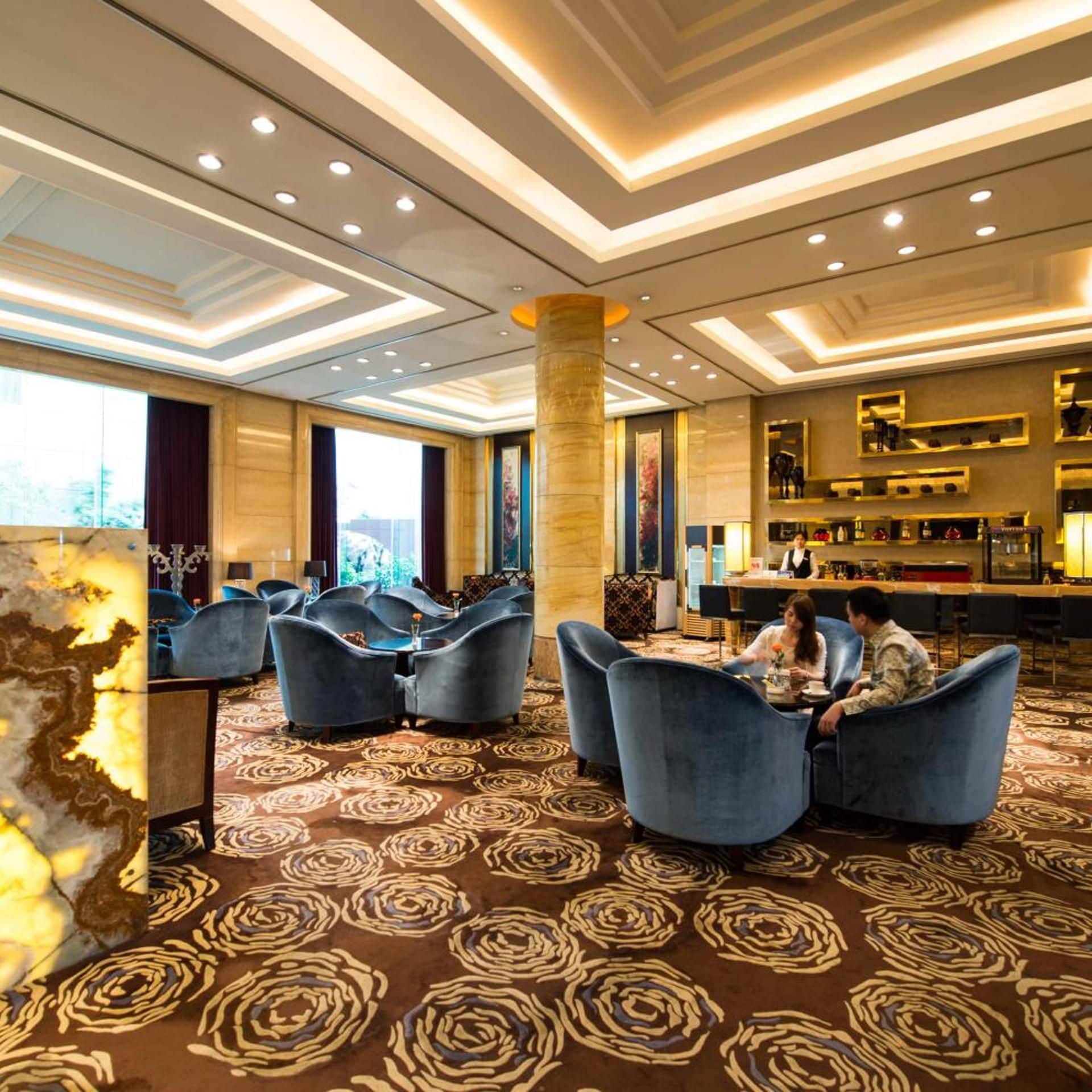 A hotel lobby with a bar area, seating arrangements, and a patterned carpet.